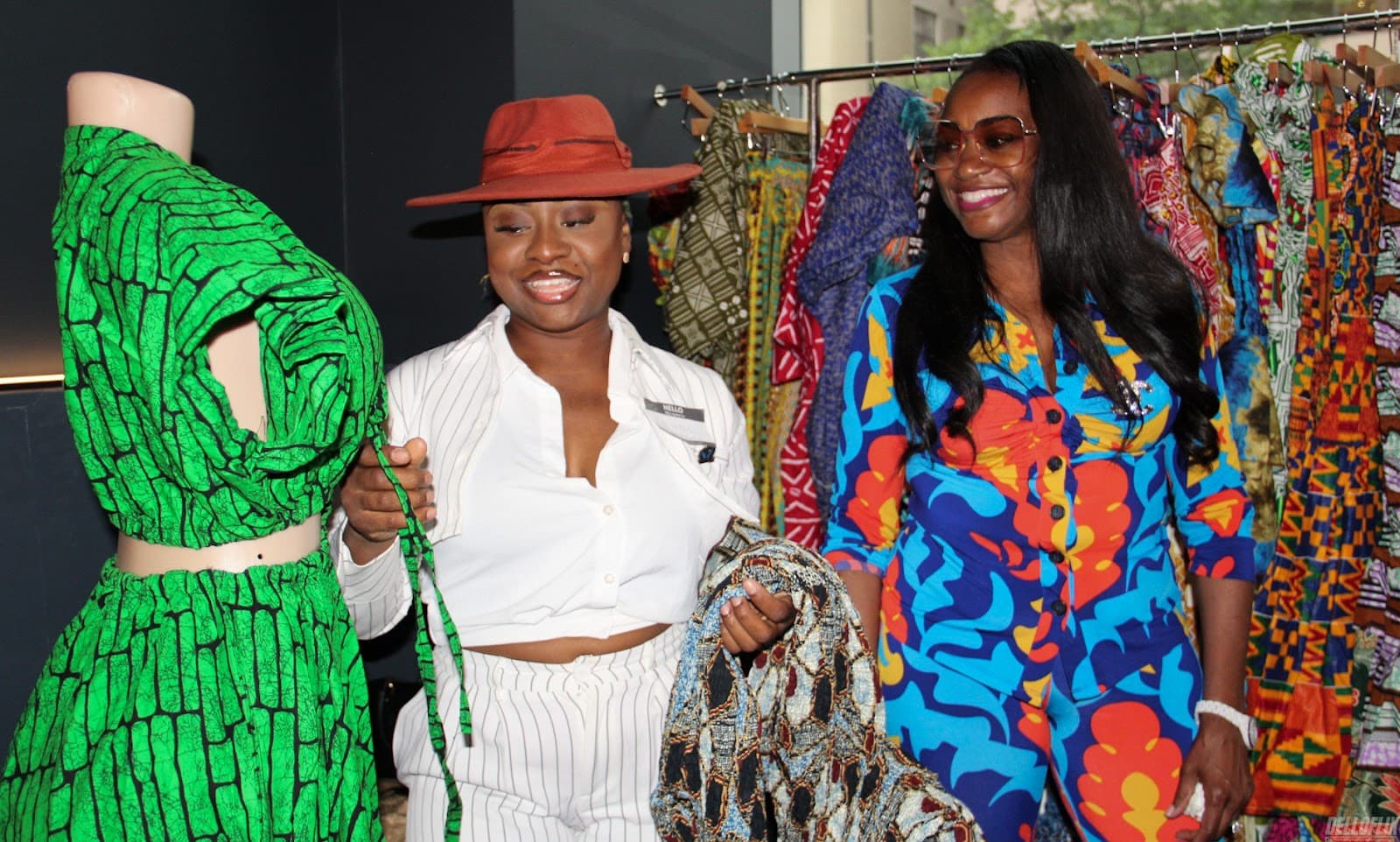 Fashion designers smiling beside colorful garments at a marketplace event