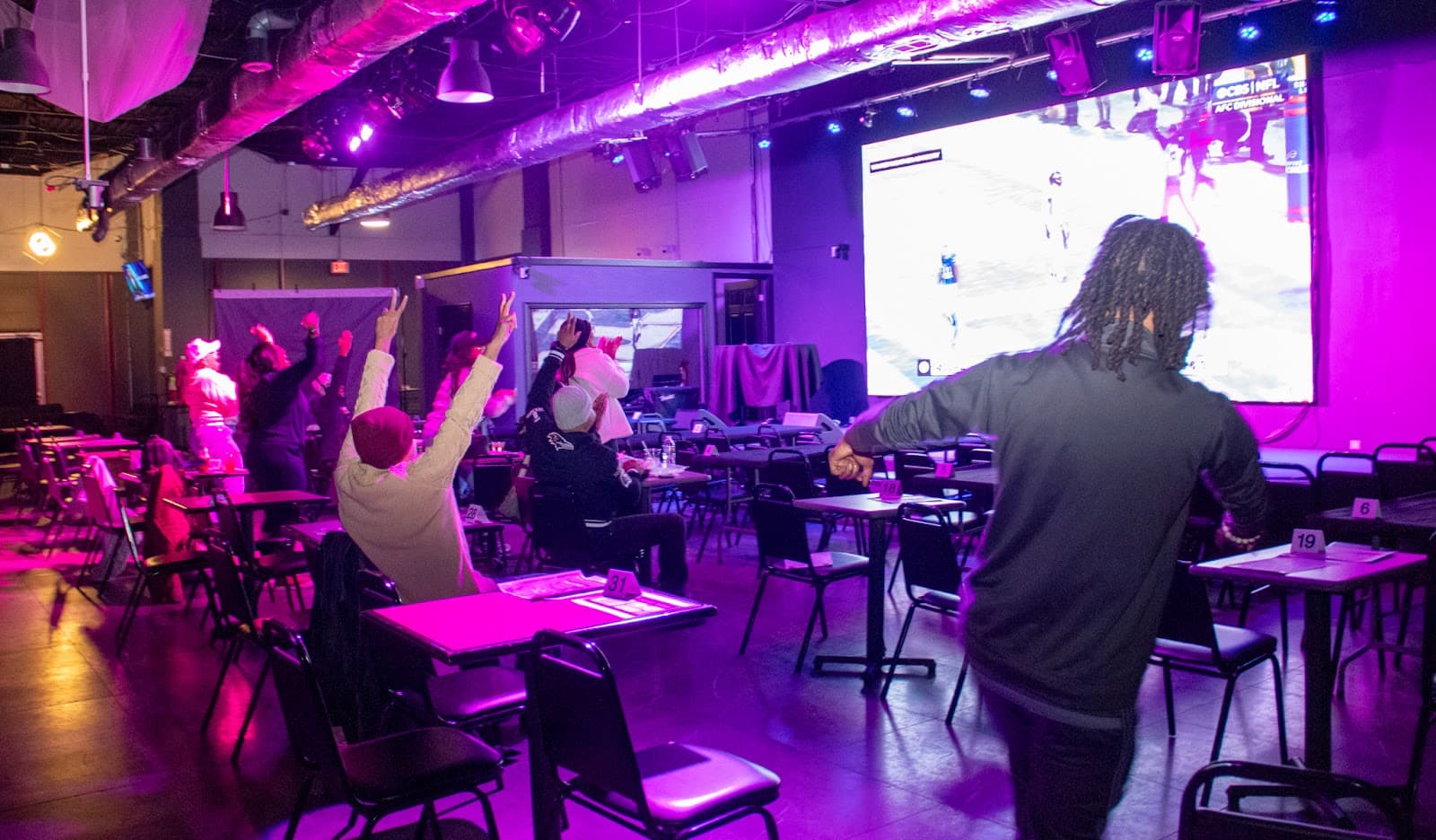 Fans celebrating in front of a giant screen at a game-day party