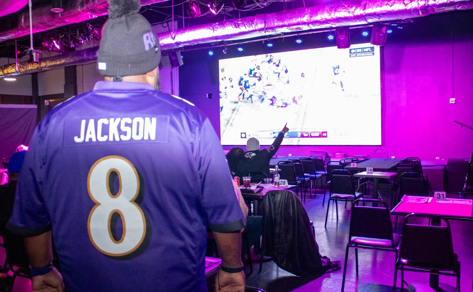 A fan in a Ravens jersey watching the game on the big screen