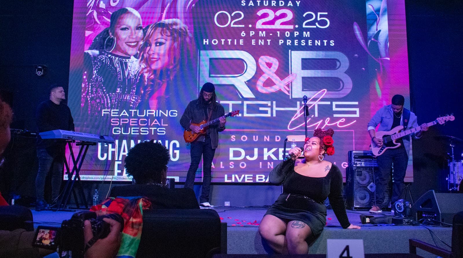 Full band and vocalists performing at an R&B night under purple light