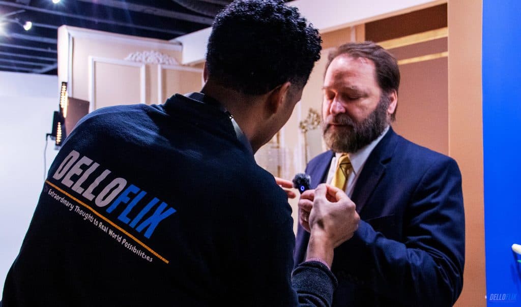 A DelloFlix crew member mic-ing up an executive before an on-camera interview