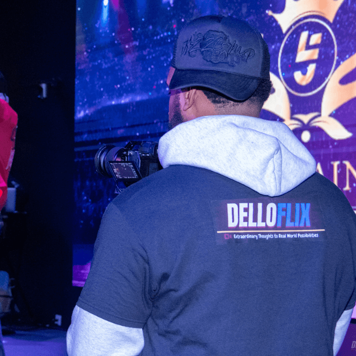 A DelloFlix camera operator in a branded tee filming a stage event