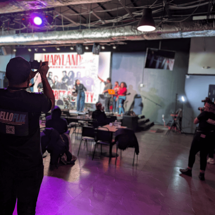 DelloFlix crew members in branded shirts filming a live comedy show from the venue floor